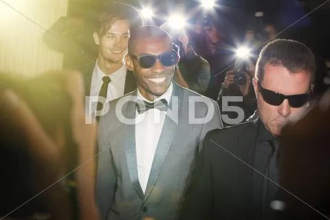 Smiling celebrity in sunglasses being photographed by paparazzi photographers at Stock Photos