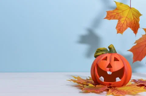Smiling ceramic pumpkin lantern on a blue background with autumn maple leaves. Foto stock