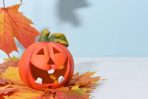 Smiling ceramic pumpkin lantern on a blue background with autumn maple leaves. Fotos de archivo