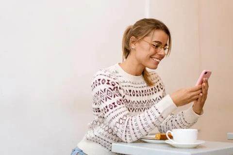 Smiling charming girl using mobile phone while drinking coffee in cafe Stock Photos