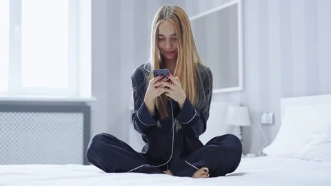 Smiling charming young woman using mobile phone sitting on bed happy at home Stock Footage 121065408