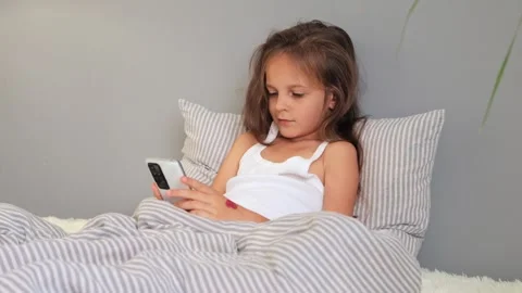 Smiling cheerful cute brown haired girl resting on pillow under blanket in .. Vidéo 252089555