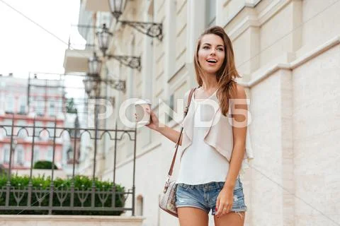 Smiling cheerful girl holding take away cup and walking outdoors Stock Photos