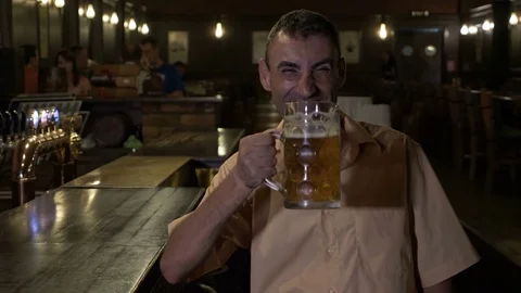 Smiling cheerful man drinks beer at the bar and cheers looking at camera Stock Footage
