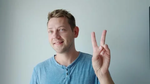 Smiling cheerful young man showing two fingers up greeting gesture, victory sign Stock-Footage 252132434