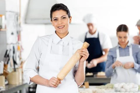 Smiling Chef Holding Rolling Pin While Colleagues Preparing Past 스톡 사진