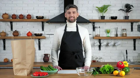 Smiling chef man in apron standing near table with food vegetables ready to cook Stock Footage 149745344