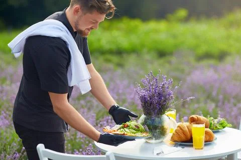 Smiling chef serving food on table in lavender field. Stock Photos