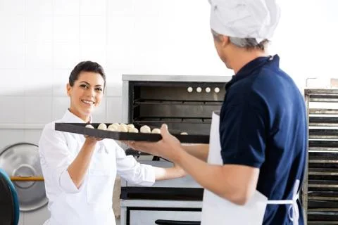 Smiling Chef Taking Baking Sheet From Colleague In Kitchen Foto stock