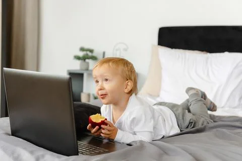 A smiling child lying on a bed next to his laptop Stock Photos