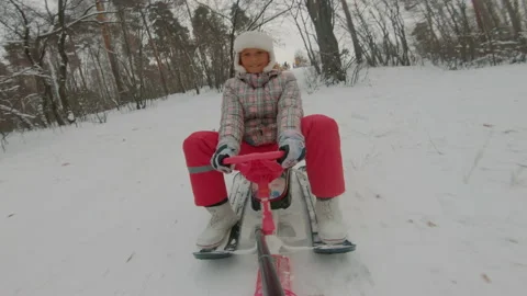 Smiling child is rolling down slide on sled, school-age girl sledding in snow Video stock 165604066