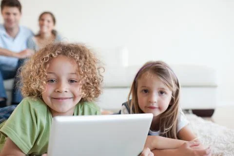 Smiling children using a tablet computer while their happy parents are watching Stock Photos