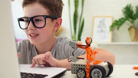 Smiling clever boy in eyeglasses programs a robot car using a laptop at home. 스톡 동영상 196792997