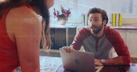 Smiling colleagues in red attire collaborating at office desk, pointing to Stock Footage 331125506