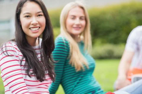 Smiling college student with blurred friend sitting in park Stock Photos