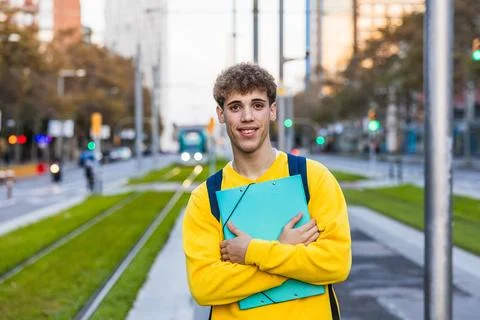 Smiling college student holding a binder and wearing backpack in urban setting Stock Photos