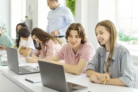 Smiling college students studying with laptops in classroom as teacher guides Stock Photos
