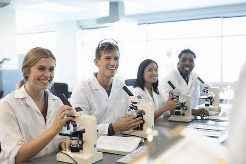 Smiling college students using microscopes, conducting scientific experiment in Stock Photos