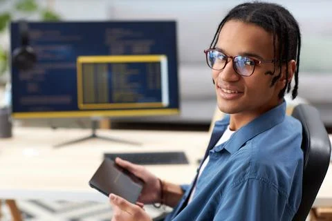 Smiling computer programmer holding tablet and looking at camera at workplace Stock-Fotos