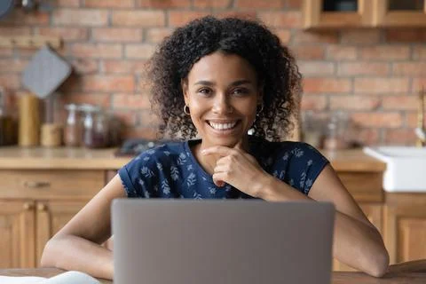 Smiling confident black lady sit by laptop at home office Stock Photos