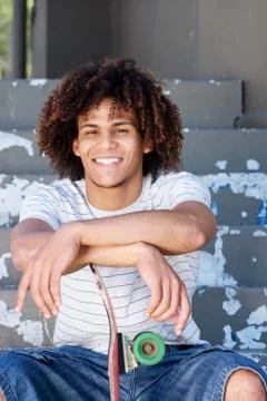 Smiling cool guy sitting outside with skateboard Stock Photos