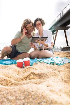 Smiling couple on the beach browsing digital tablet and smartphone apps.Vertical Stock Photos