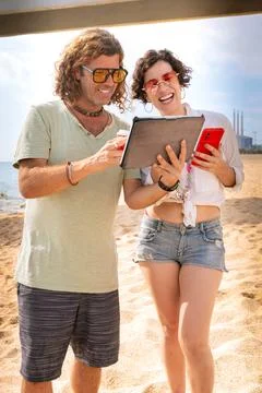 Smiling couple on the beach browsing digital tablet and smartphone apps. Stock Photos