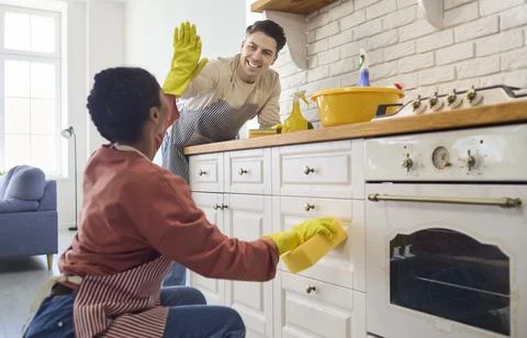 Smiling couple doing kitchen cleaning chores, teamwork high five and home Stock Photos