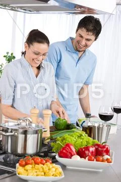 Smiling couple drink red wine cooking in kitchen Stock Photos