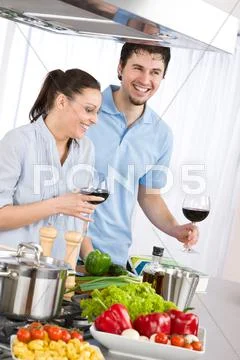 Smiling couple drink red wine cooking in kitchen Stock Photos
