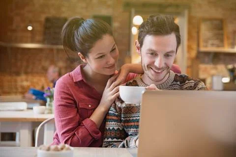 Smiling couple drinking coffee using laptop at cafe Stock Photos