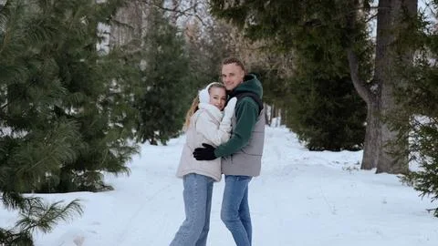 Smiling couple embracing while walking through snow covered evergreen forest Stock Photos