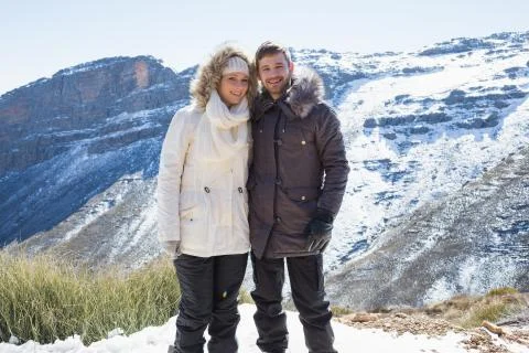 Smiling couple in fur hood jackets against snowed mountain range Stock Photos