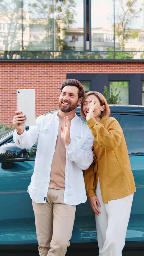 Smiling couple having a video chat with friends during an EV charging stop in an Stock Footage 327545921