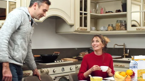 A smiling couple on a kitchen. Man serving woman a cup of tea and sitting near Stock Footage 145141916