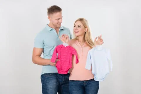 Smiling couple looking at each other while holding baby clothing over white b Fotos Stock