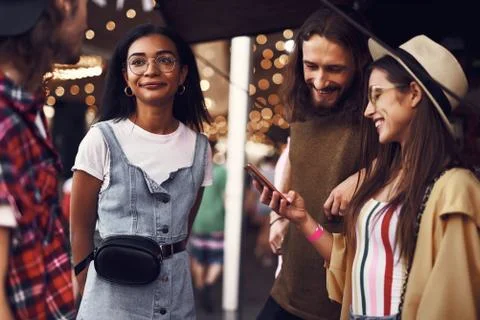 Smiling couple looking at smartphone while their friends talking Stock-Fotos