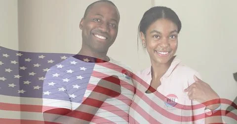 Smiling couple posing at wall, striped tee, pink top, showing I Voted stickers, Fotos Stock