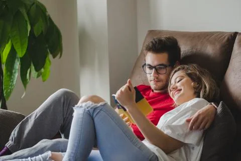 Smiling couple reading book while resting on sofa in living room at home Stock Photos