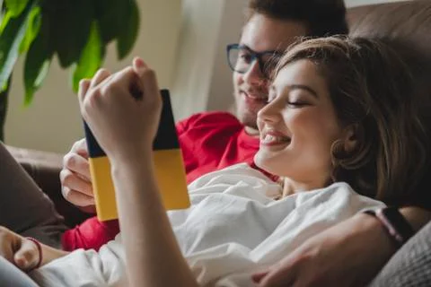 Smiling couple reading book while resting on sofa in living room at home Stock Photos
