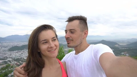 Smiling couple recording video, taking selfie in the mountains. Man kisses girl Stock Footage 76509944