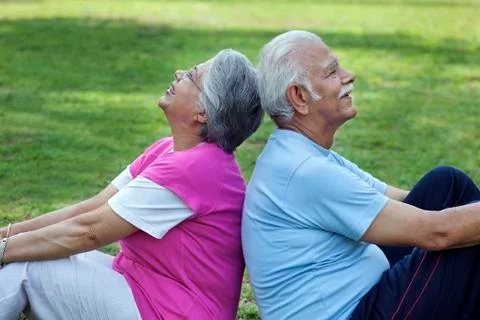 Smiling couple sitting back to back in a park Stock Photos