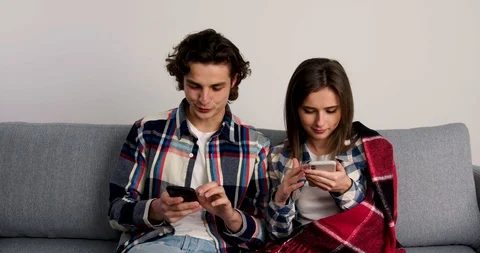 Smiling couple sitting on sofa and talking while using smartphones Stock Footage 123965953