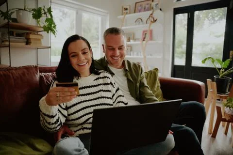 Smiling couple using debit card to make online purchase transaction at home Stock Photos