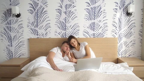 Smiling couple using a laptop lying on their bed Stock Footage 73993993