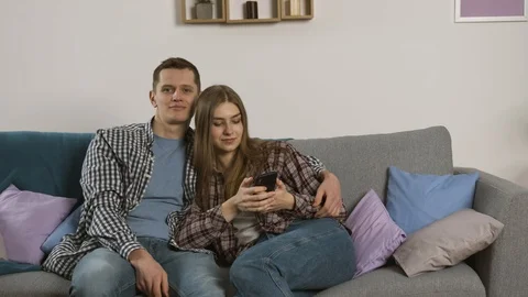 Smiling couple using smartphone and watching tv together 스톡 동영상 125320637