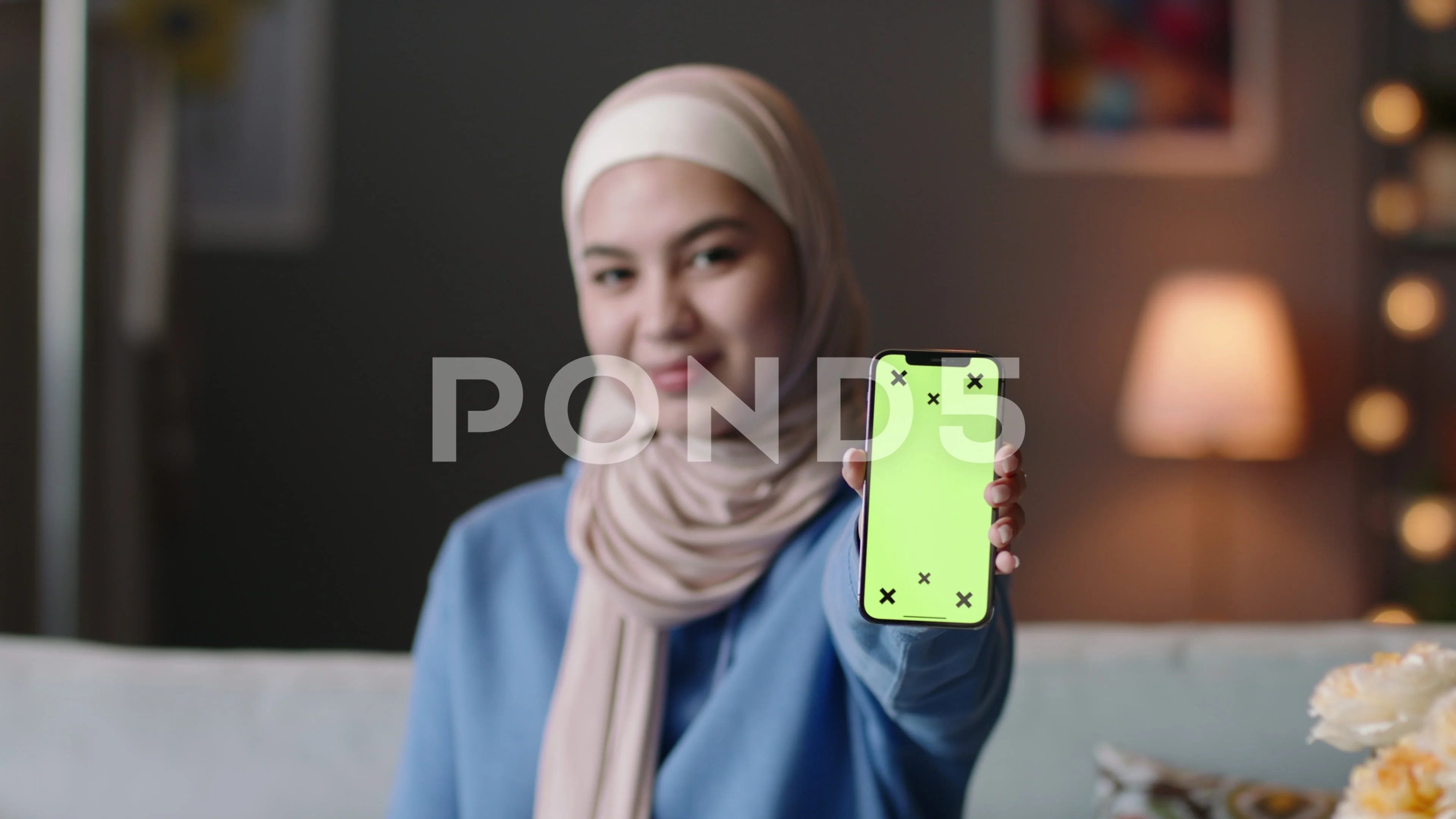 Smiling covered Muslim woman in hijab showing smartphone screen with chroma  key