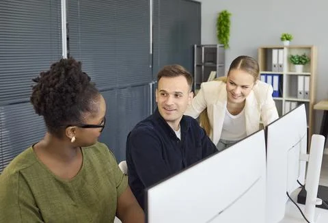 Smiling coworkers collaborating at computers in modern office, business teamwork Foto stock