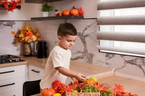 Smiling cute sitting on kitchen table with fruits, autumn leaves and pumpkin Stock Photos