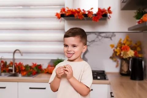 Smiling cute sitting on kitchen table with fruits, autumn leaves and pumpkin Stock Photos